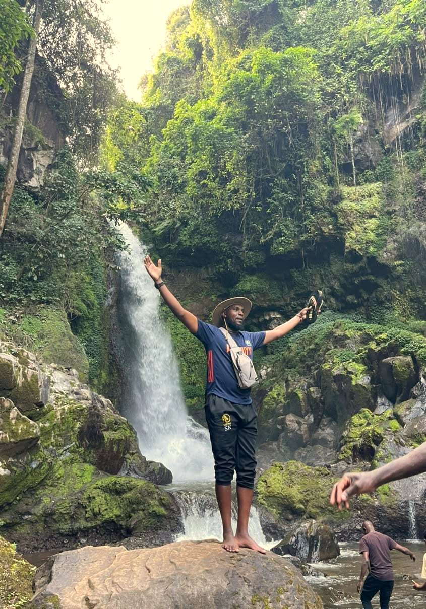 A traveller with arms raised in celebration in front of a waterfall